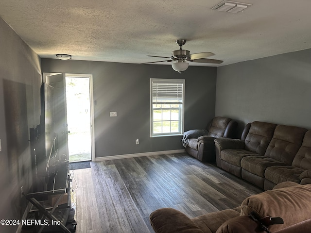 living room featuring ceiling fan, dark wood-type flooring, and a textured ceiling