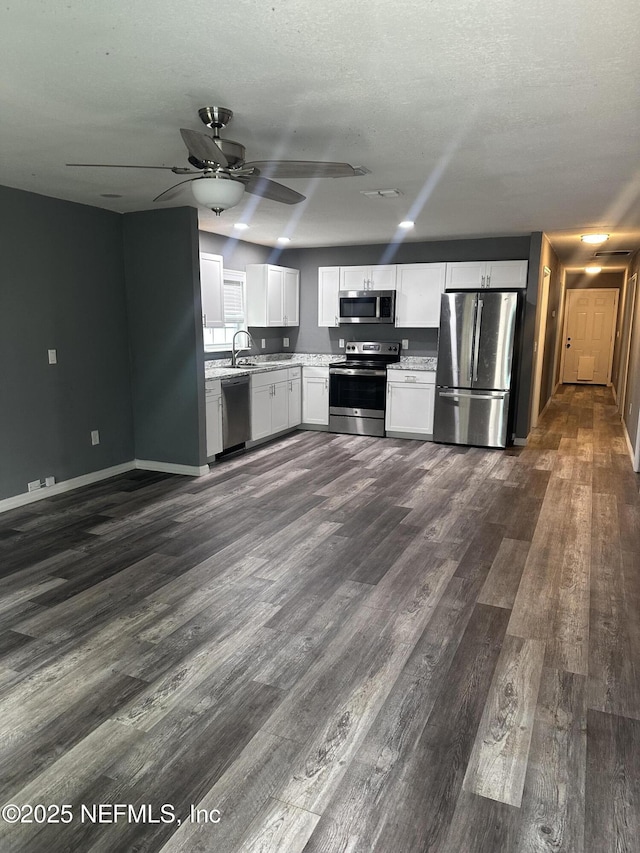 kitchen with appliances with stainless steel finishes, dark hardwood / wood-style floors, sink, white cabinets, and ceiling fan