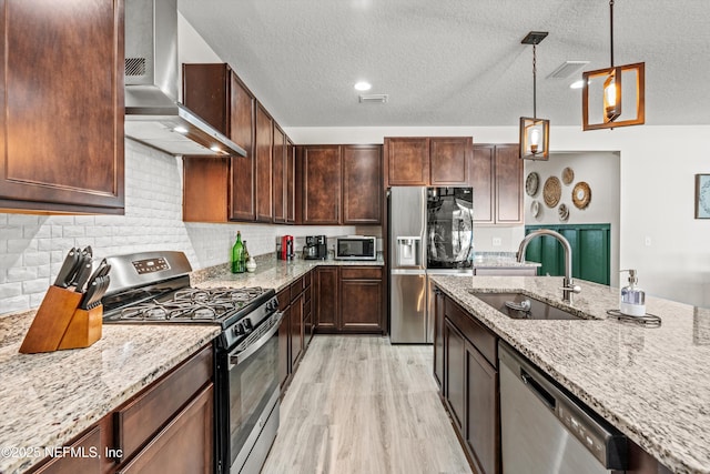 kitchen with sink, wall chimney exhaust hood, a textured ceiling, appliances with stainless steel finishes, and light stone counters