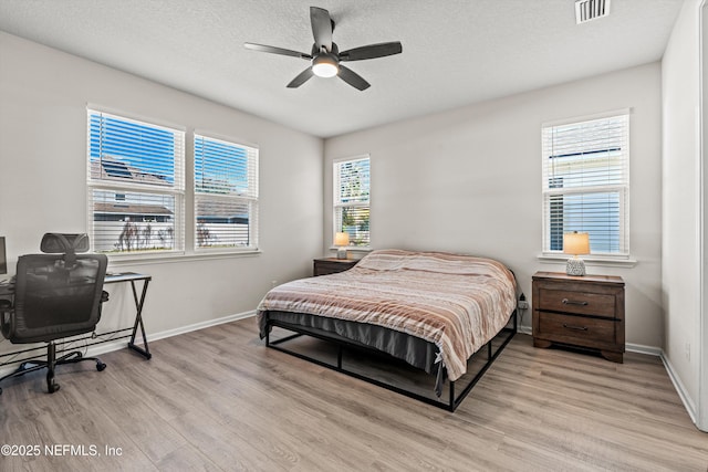 bedroom featuring multiple windows, a textured ceiling, light wood-type flooring, and ceiling fan