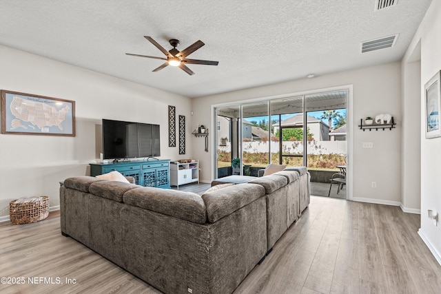 living room with ceiling fan, light wood-type flooring, and a textured ceiling