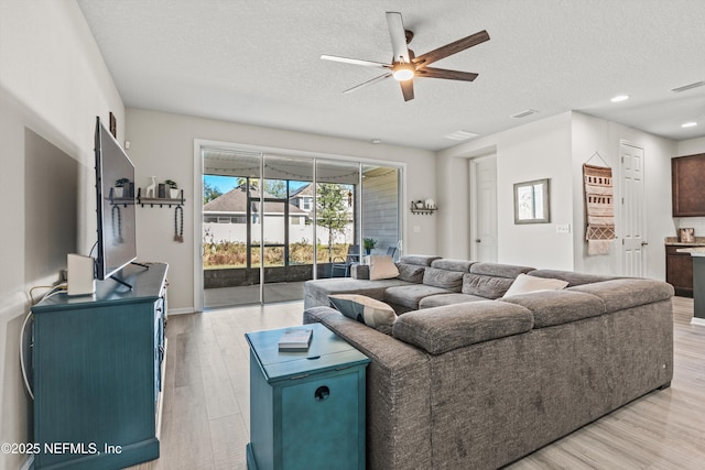 living room featuring ceiling fan, light hardwood / wood-style floors, and a textured ceiling