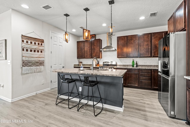 kitchen featuring dark brown cabinetry, stainless steel appliances, sink, wall chimney range hood, and a center island with sink