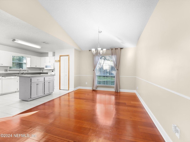 unfurnished dining area with a healthy amount of sunlight, light wood-type flooring, a textured ceiling, and an inviting chandelier