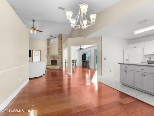 kitchen featuring gray cabinetry, vaulted ceiling, white fridge with ice dispenser, a fireplace, and light hardwood / wood-style floors