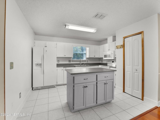 kitchen with white appliances, sink, light tile patterned floors, a kitchen island, and white cabinetry