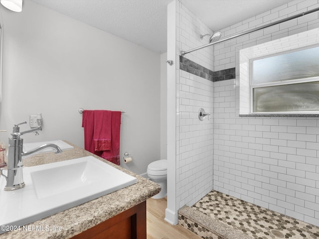 bathroom with a textured ceiling, tiled shower, toilet, vanity, and hardwood / wood-style flooring