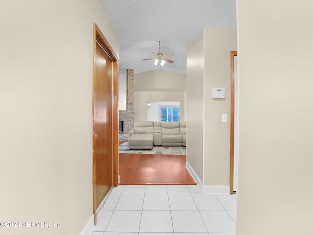 corridor with a textured ceiling, light tile patterned flooring, and lofted ceiling