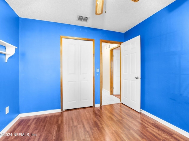 unfurnished bedroom with a closet, hardwood / wood-style floors, ceiling fan, and a textured ceiling