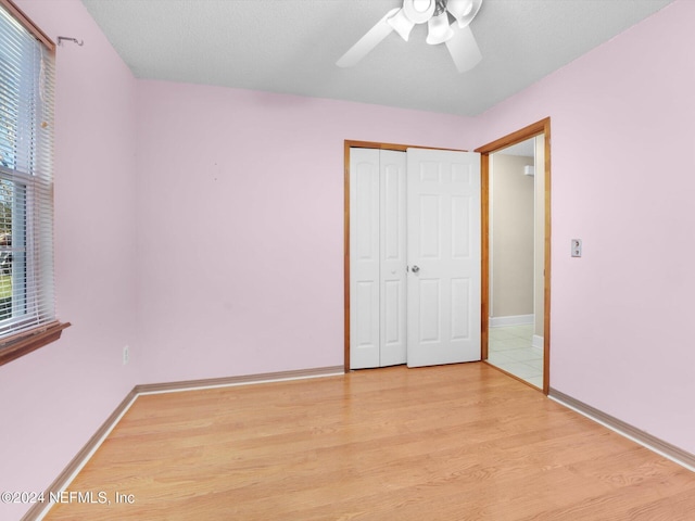 unfurnished bedroom featuring ceiling fan, light wood-type flooring, a textured ceiling, and a closet