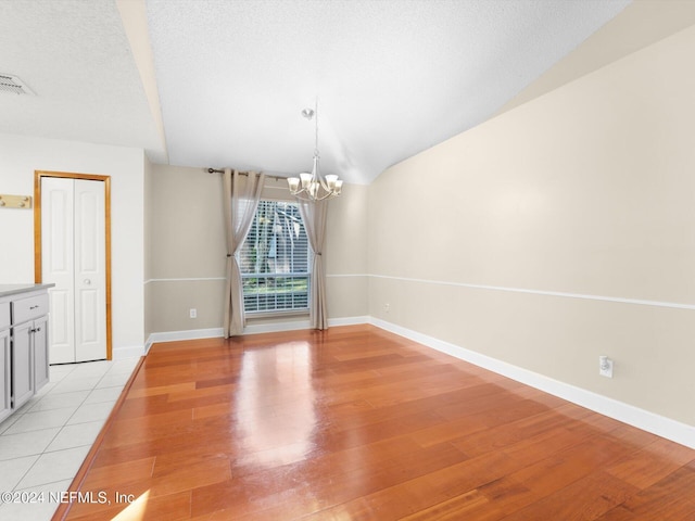 unfurnished dining area with a textured ceiling, a chandelier, vaulted ceiling, and light hardwood / wood-style floors