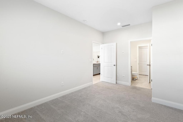 unfurnished bedroom with ensuite bath and light colored carpet