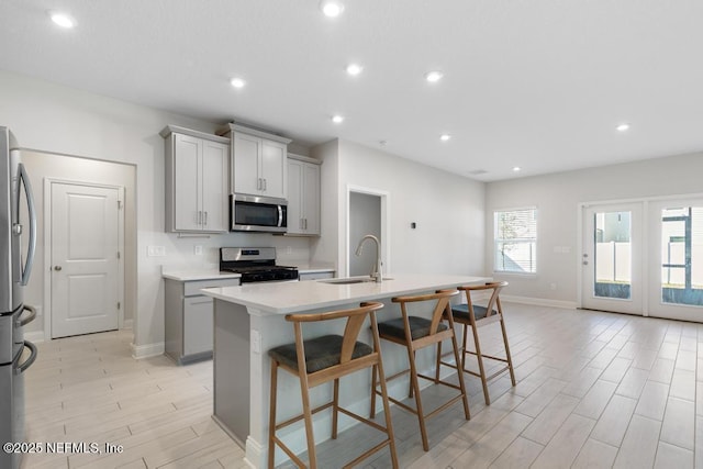 kitchen featuring gray cabinetry, a kitchen island with sink, a kitchen breakfast bar, sink, and appliances with stainless steel finishes