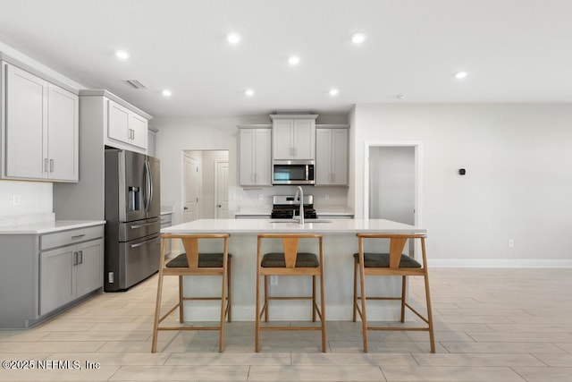 kitchen featuring a breakfast bar, gray cabinets, a kitchen island with sink, and appliances with stainless steel finishes