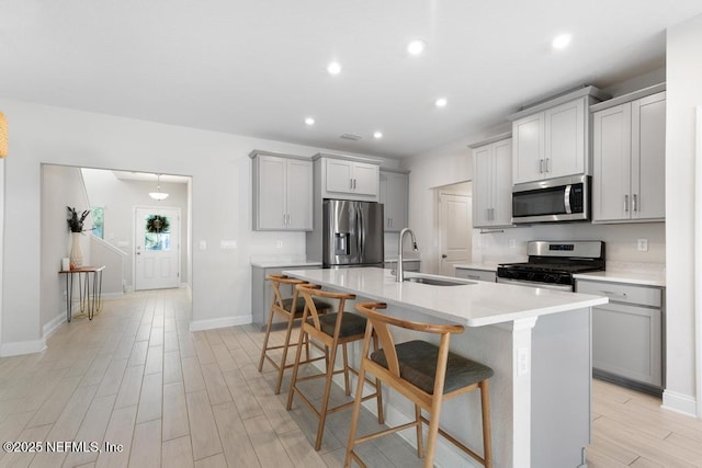 kitchen featuring sink, a kitchen breakfast bar, an island with sink, gray cabinets, and appliances with stainless steel finishes