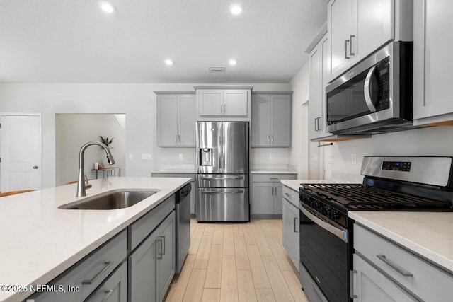 kitchen featuring appliances with stainless steel finishes, light wood-type flooring, light stone counters, gray cabinetry, and sink