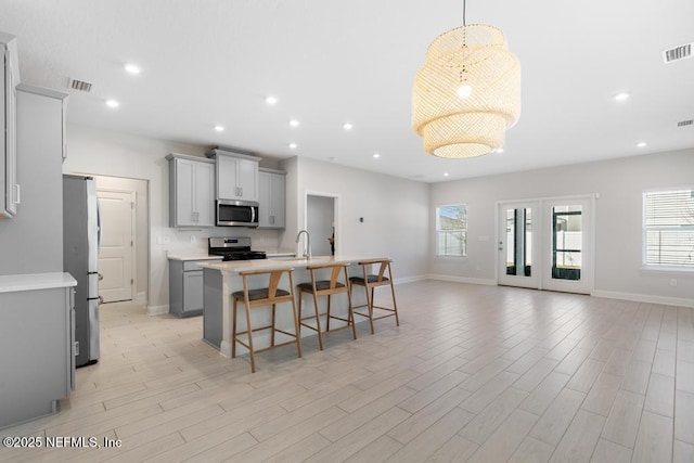 kitchen featuring a kitchen bar, stainless steel appliances, gray cabinets, hanging light fixtures, and an island with sink