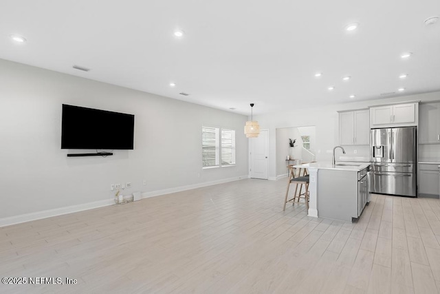 kitchen featuring a center island with sink, white cabinets, stainless steel fridge, light hardwood / wood-style floors, and a kitchen bar