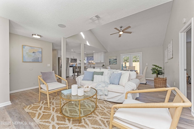 living room with ceiling fan, french doors, a textured ceiling, lofted ceiling, and light wood-type flooring