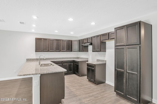 kitchen with kitchen peninsula, light stone counters, dark brown cabinetry, sink, and light hardwood / wood-style flooring