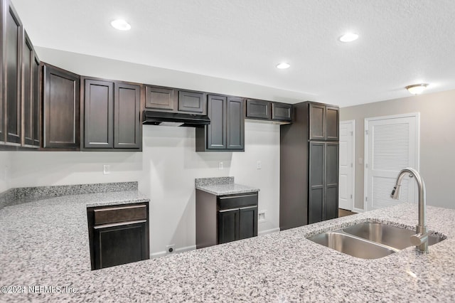 kitchen with light stone countertops, dark brown cabinetry, and sink