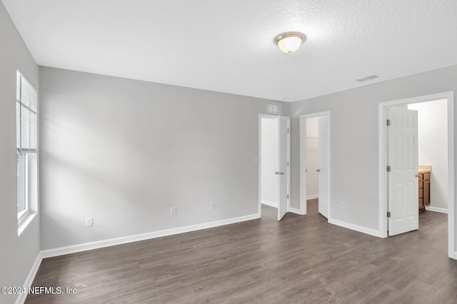 unfurnished bedroom featuring ensuite bathroom, dark wood-type flooring, and a textured ceiling