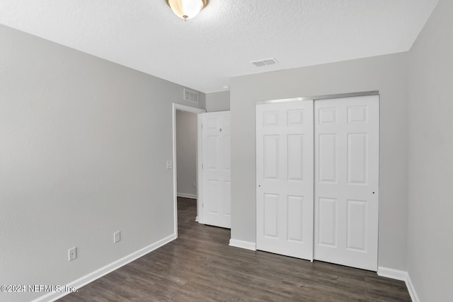 unfurnished bedroom featuring dark hardwood / wood-style floors, a textured ceiling, and a closet