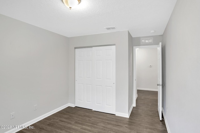 unfurnished bedroom with a textured ceiling, a closet, and dark hardwood / wood-style floors