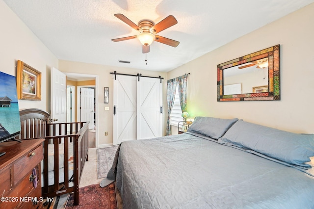 bedroom with ceiling fan, carpet flooring, a barn door, and a textured ceiling