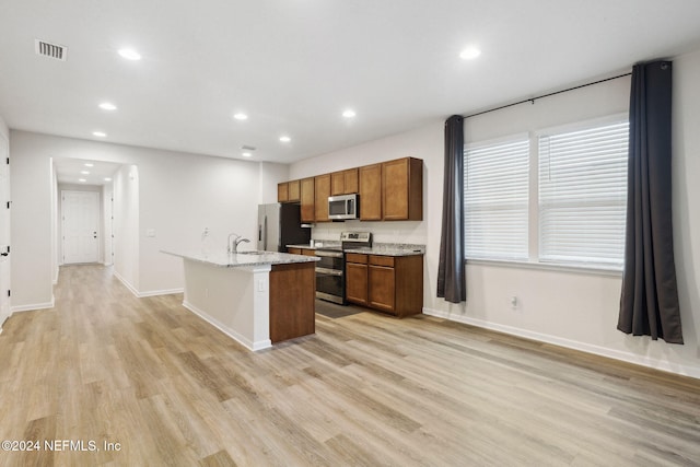 kitchen featuring a center island with sink, sink, light stone countertops, light wood-type flooring, and stainless steel appliances