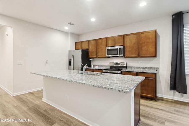 kitchen with appliances with stainless steel finishes, light wood-type flooring, a center island with sink, and sink