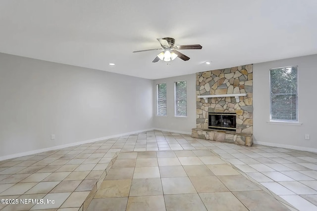 unfurnished living room with a stone fireplace, light tile patterned floors, and ceiling fan