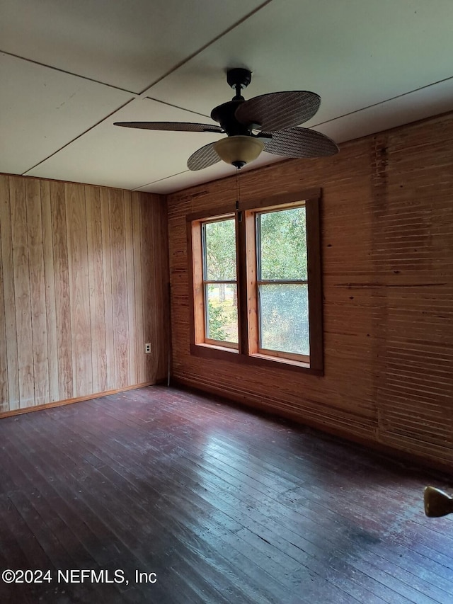 empty room with hardwood / wood-style flooring, ceiling fan, and wood walls