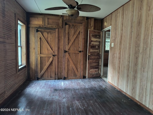 interior space with dark wood-type flooring, ceiling fan, and wooden walls