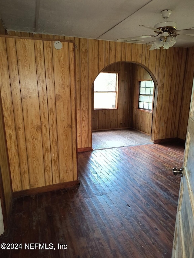 spare room featuring ceiling fan, dark wood-type flooring, and wood walls