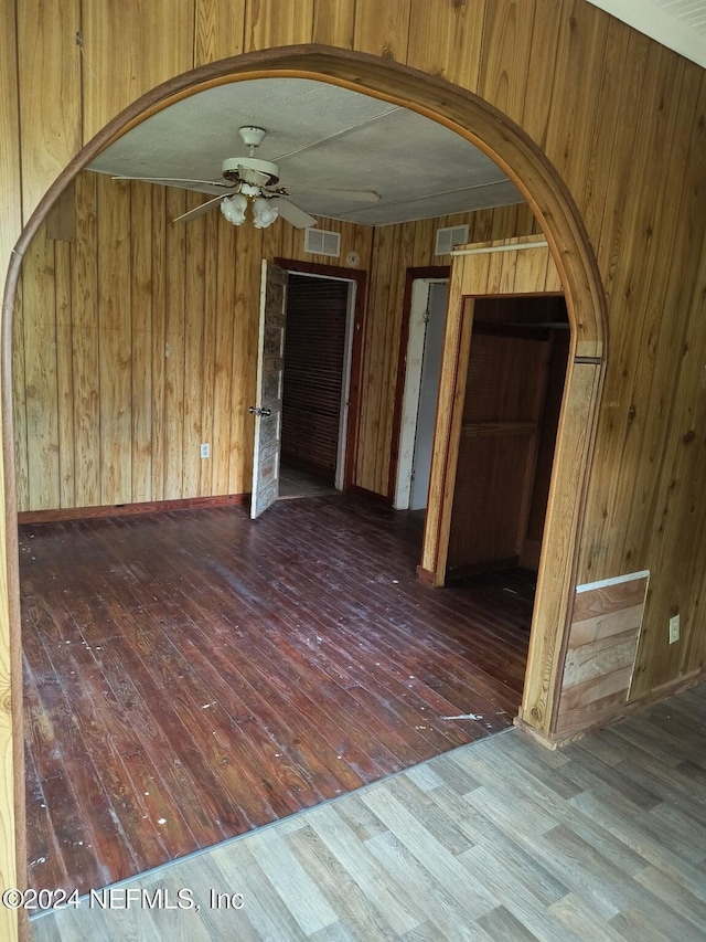 empty room featuring hardwood / wood-style flooring, ceiling fan, and wood walls