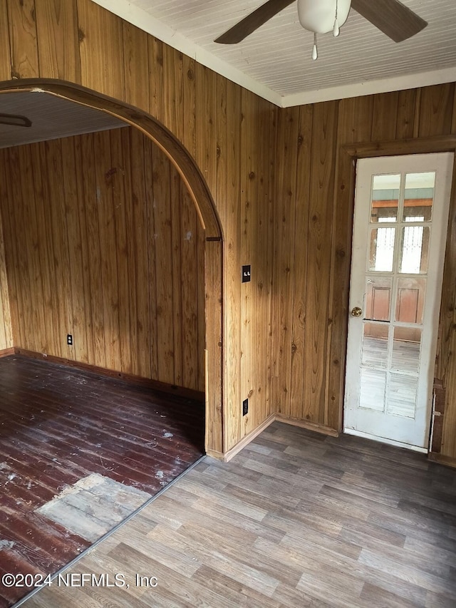 empty room with ceiling fan, wood walls, and hardwood / wood-style flooring