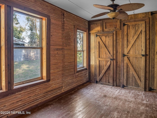 empty room featuring a wealth of natural light, wood walls, and ceiling fan