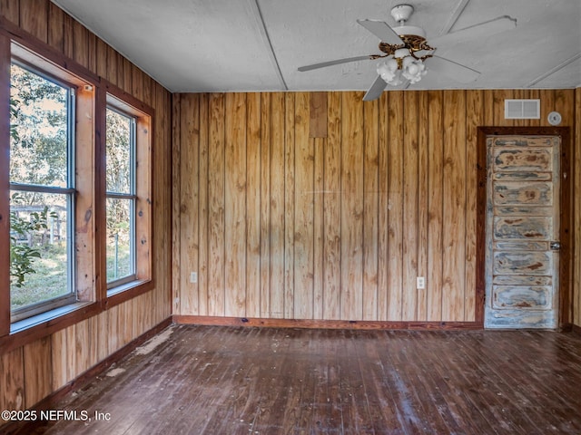 unfurnished room with a textured ceiling, wooden walls, ceiling fan, and dark hardwood / wood-style floors