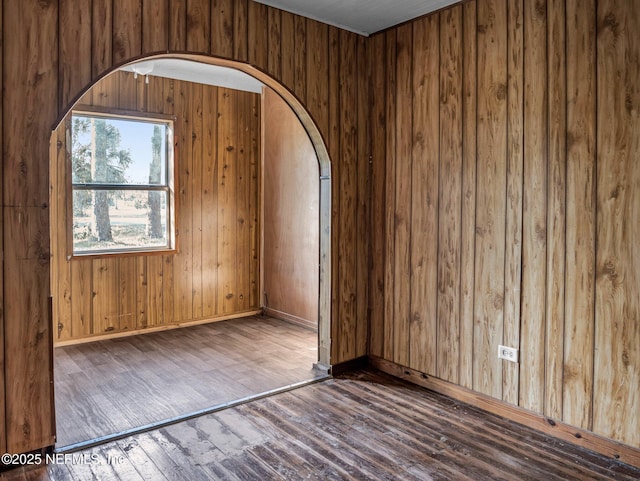 spare room featuring wooden walls and dark wood-type flooring