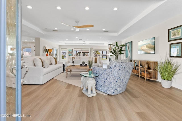 living room with light hardwood / wood-style flooring, a raised ceiling, and ceiling fan