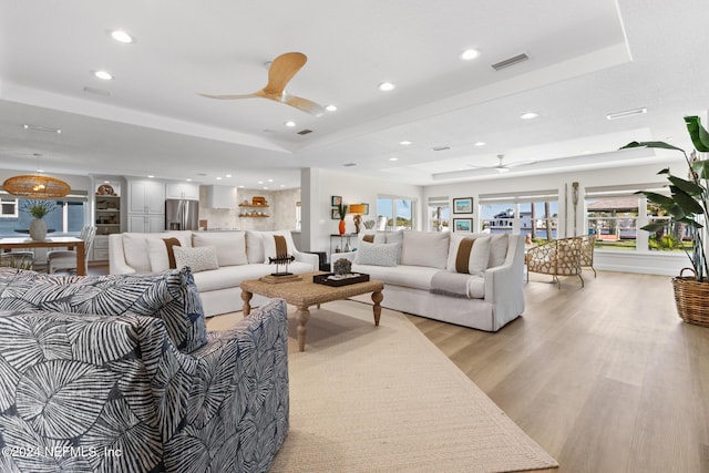 living room with ceiling fan, light hardwood / wood-style floors, and a tray ceiling