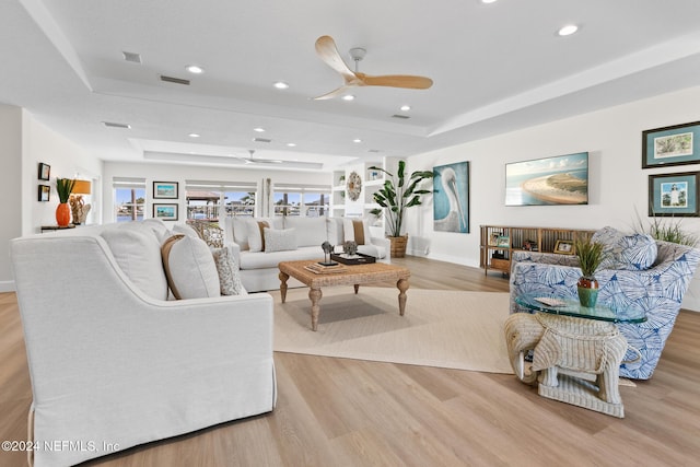 living room featuring a tray ceiling, ceiling fan, and light hardwood / wood-style floors