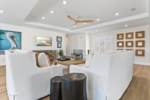 living room with a tray ceiling, ceiling fan, and hardwood / wood-style flooring