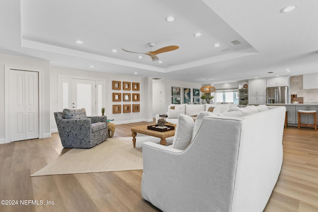 living room featuring light hardwood / wood-style floors, a raised ceiling, and ceiling fan