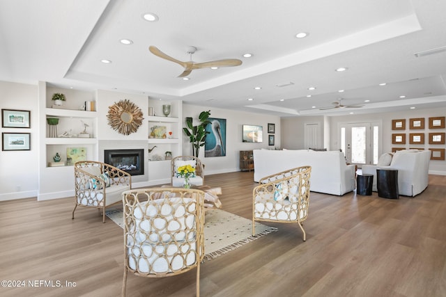 living room with a raised ceiling, ceiling fan, built in features, and hardwood / wood-style floors