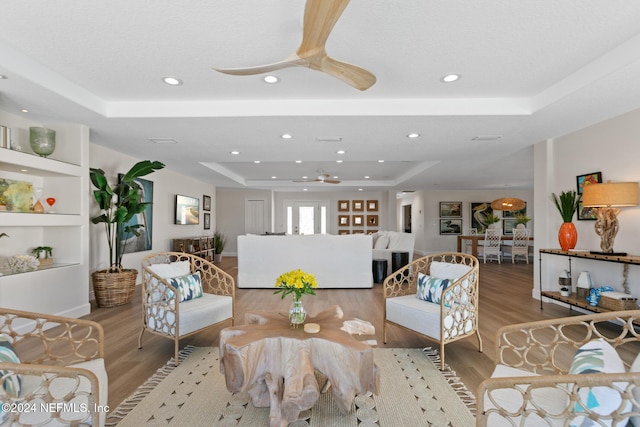 living room with light hardwood / wood-style floors, a raised ceiling, and built in features