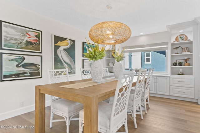 dining space with light wood-type flooring, an inviting chandelier, and built in features