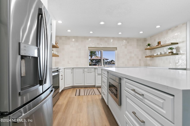 kitchen featuring backsplash, a textured ceiling, stainless steel appliances, light hardwood / wood-style flooring, and white cabinets