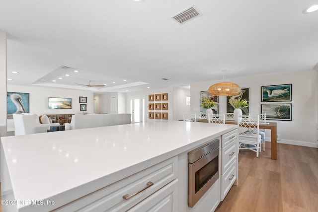 kitchen with pendant lighting, stainless steel microwave, white cabinets, a raised ceiling, and ceiling fan